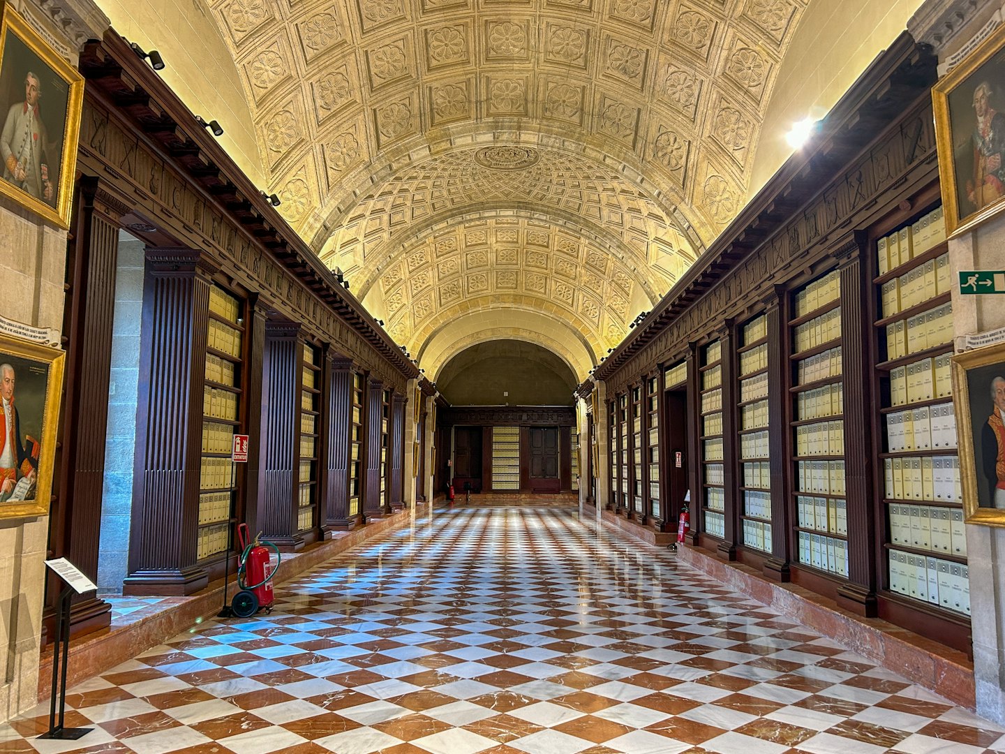 Corridoio di una biblioteca storica con librerie imponenti e soffitto decorato.