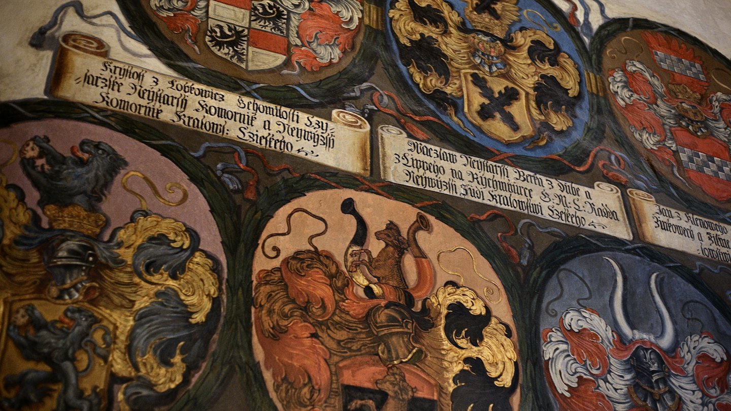 Intricata pittura murale con molteplici stemmi araldici storici dettagliati.