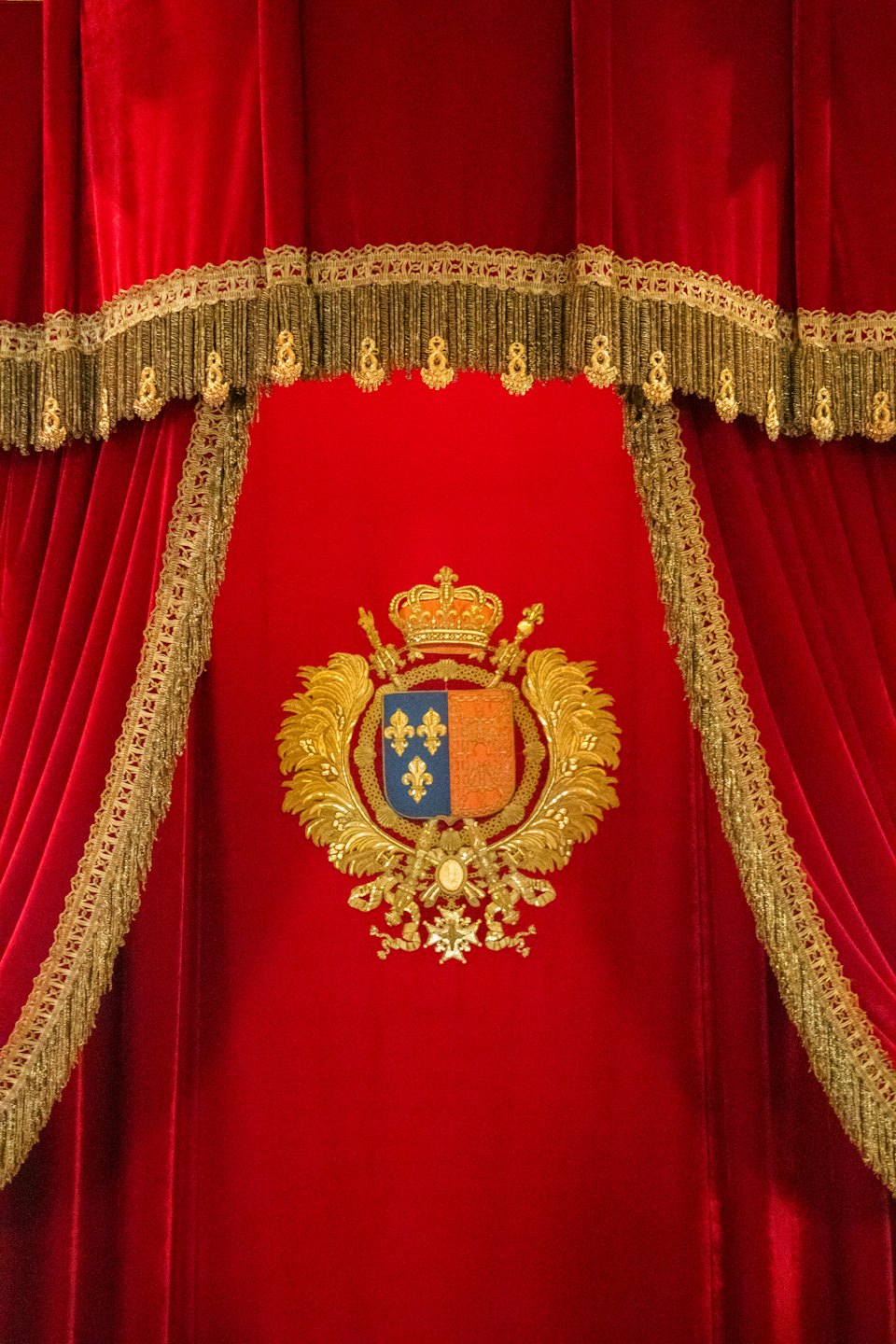 Stemma reale dorato e ornato su tende di velluto rosso scuro.